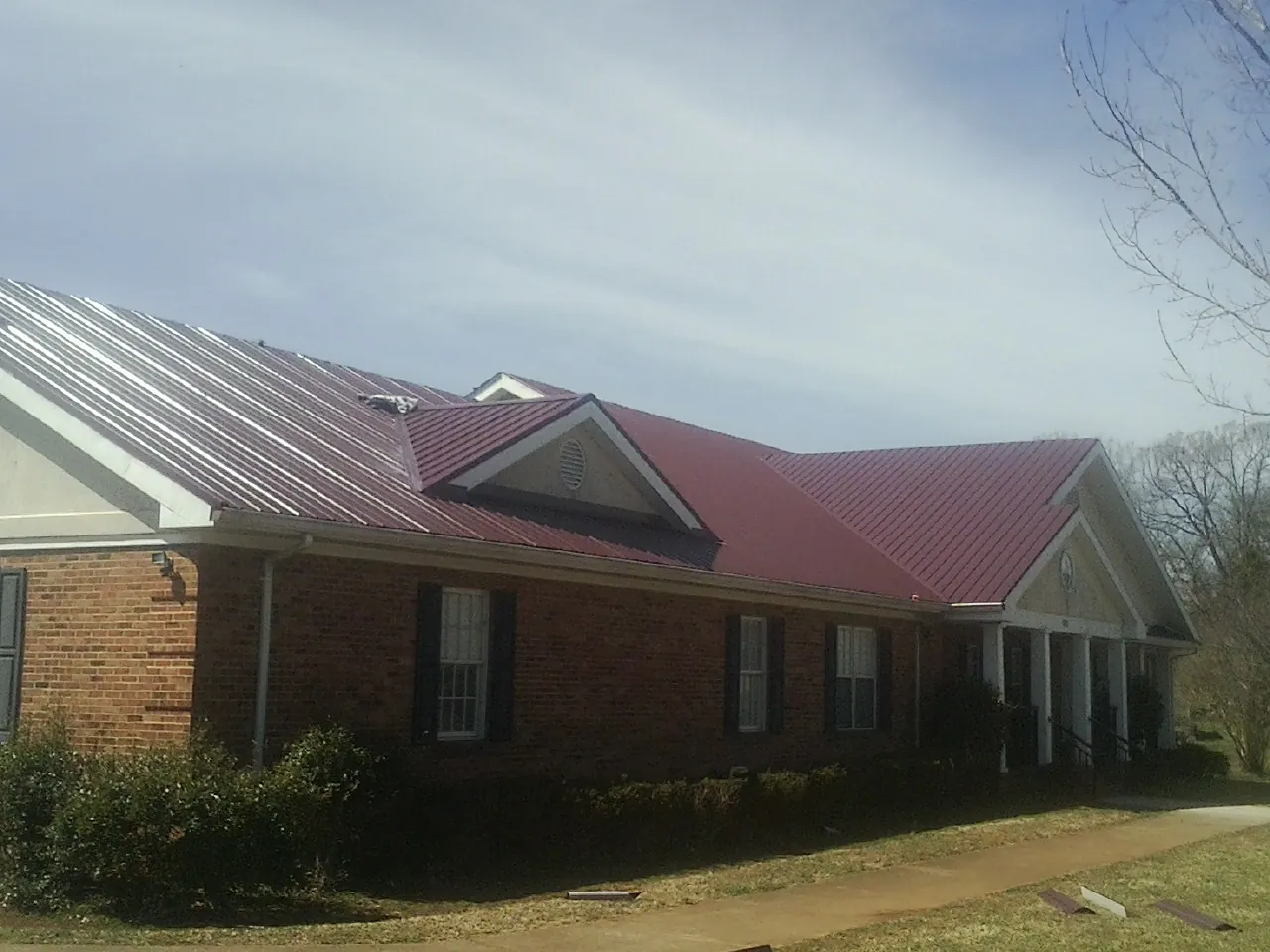 Red metal roof with gabled entries on a long brick building, from a Hail Damage Roof Repair job in March Air Reserve Base