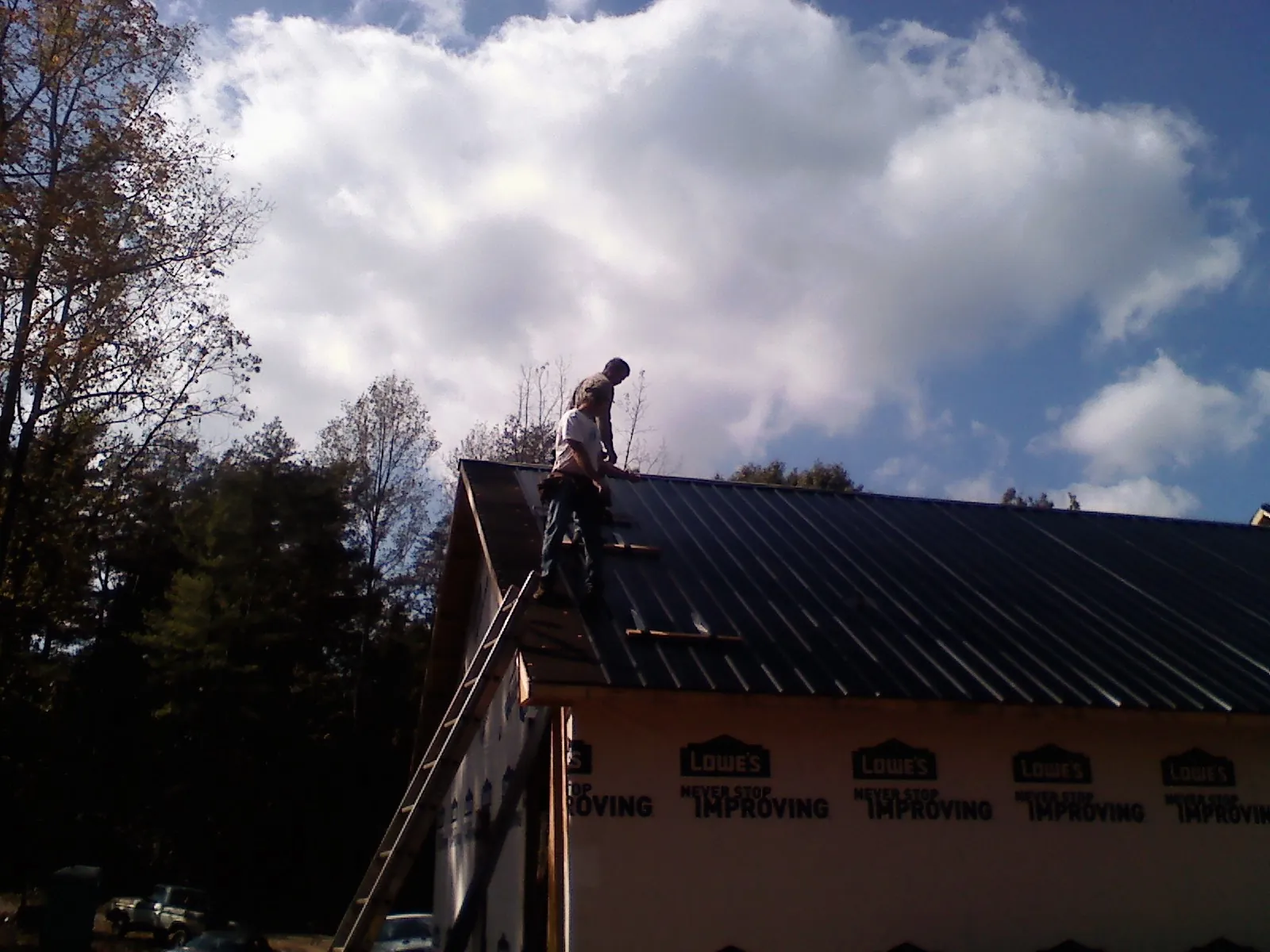 Roofer fastening dark metal panels high against a cloudy sky, from a Roof Inspection job in March Air Reserve Base