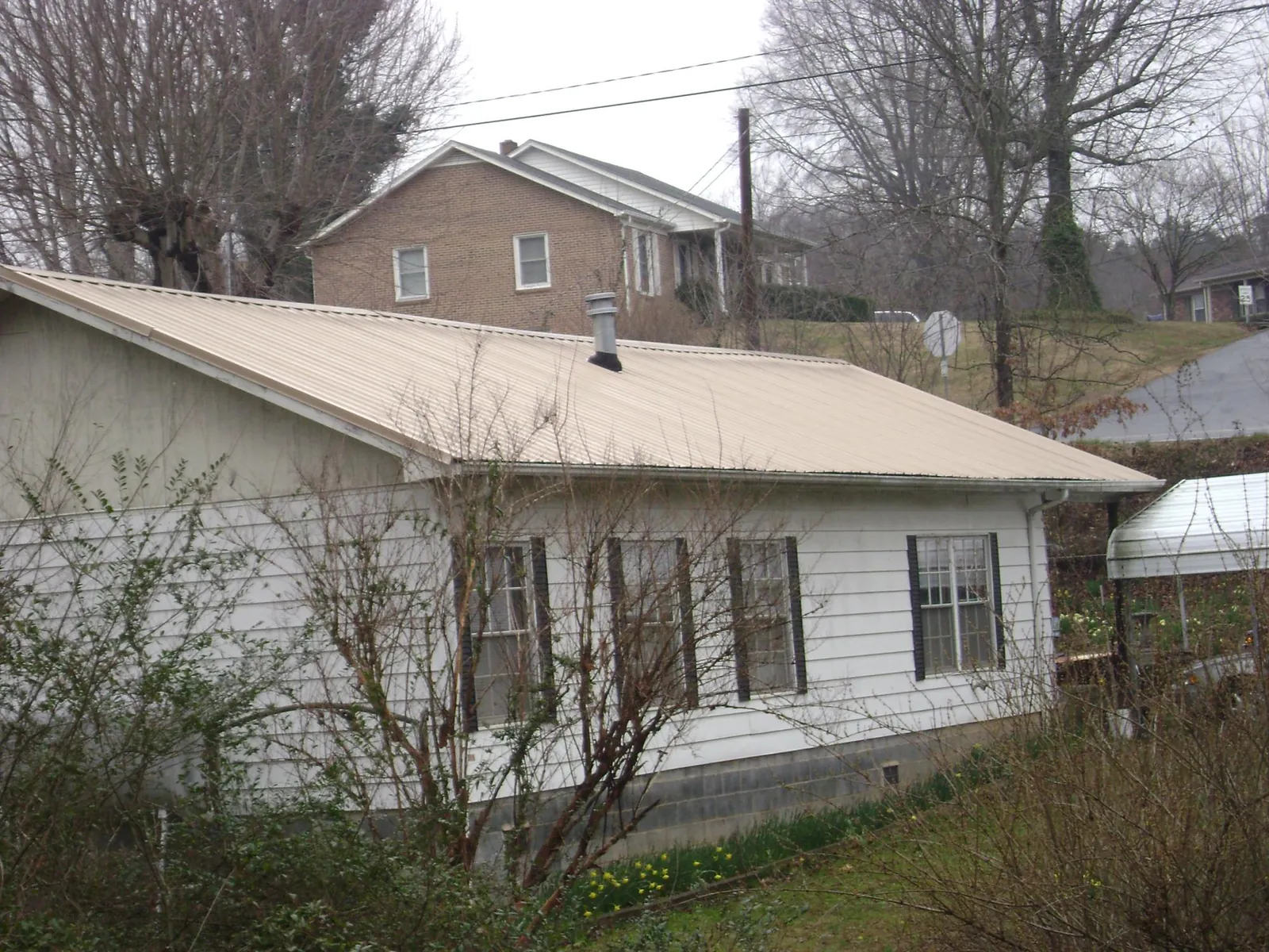 Tan metal roof on a white sided house set into a hillside — Commercial Roofing by Roofing Brothers in March Air Reserve Base